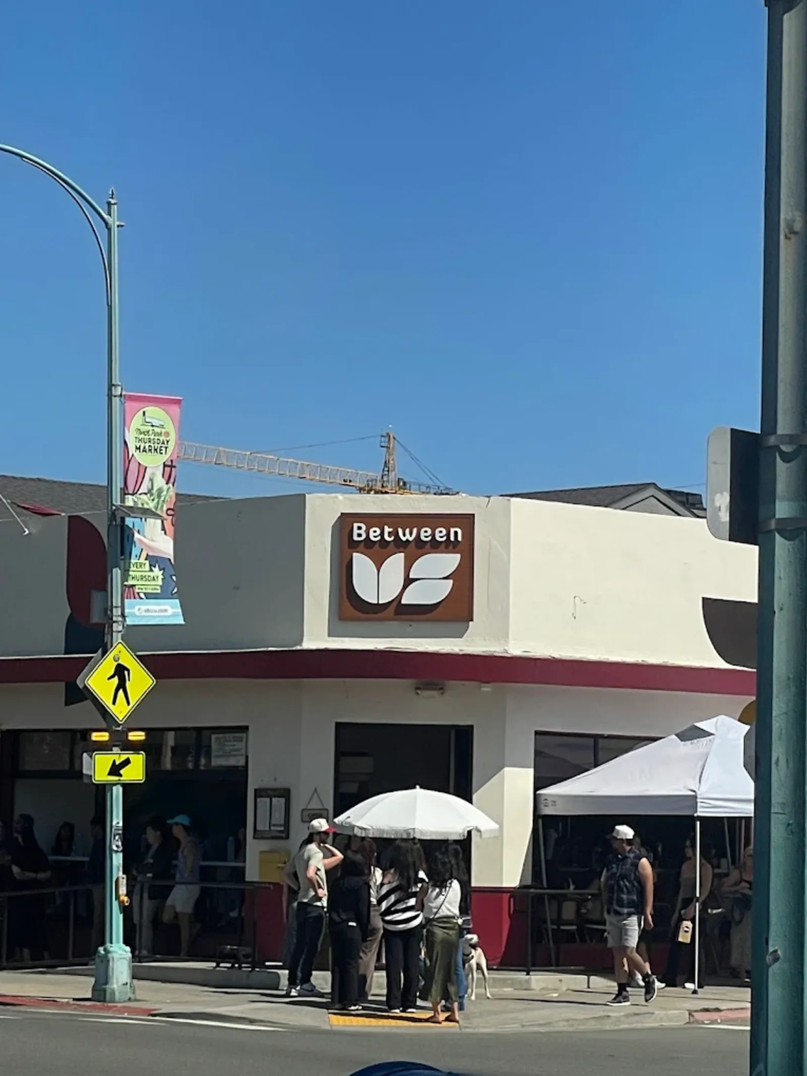A crowd gathered outside Between Us on the corner in North Park on a sunny morning