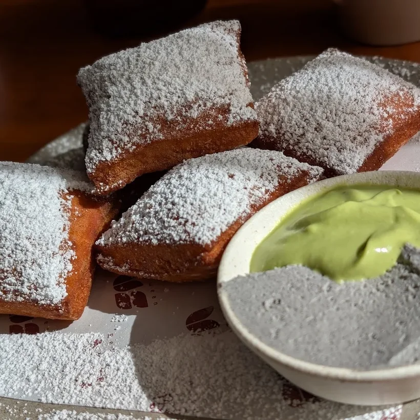 Warm beignets dusted with powdered sugar beside a matcha cream dip