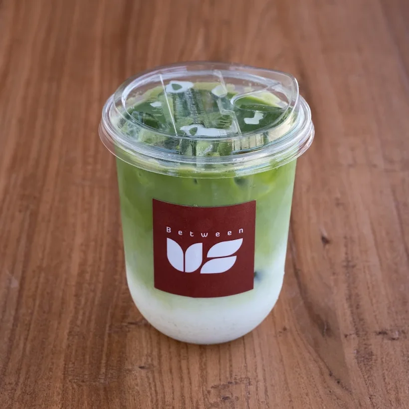 An iced house matcha latte in a cup with the Between Us label