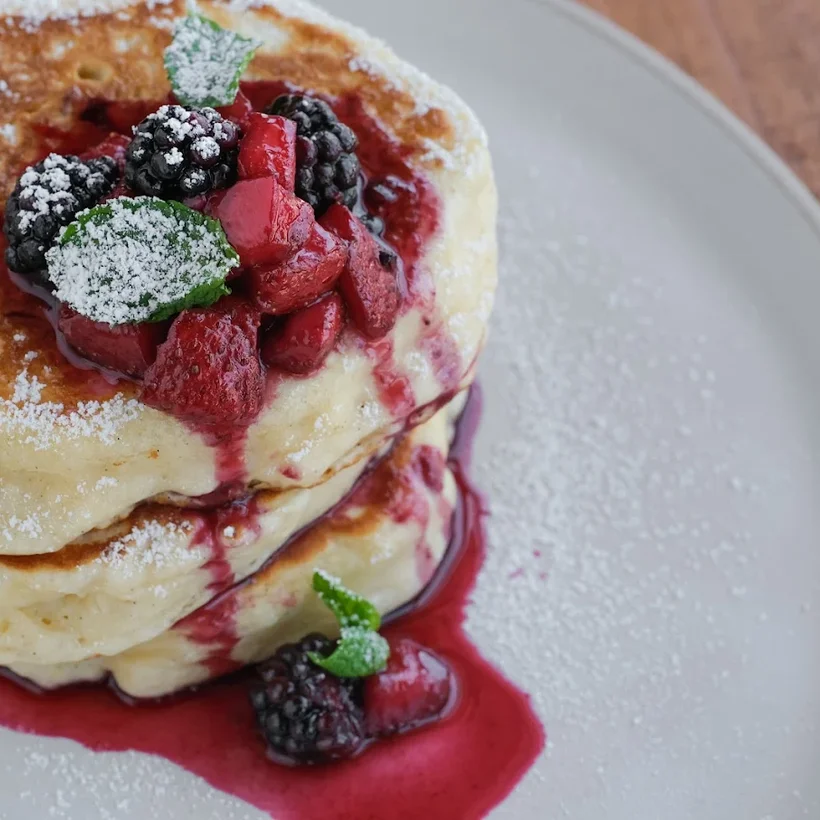 A tall stack of ricotta pancakes with berry compote and powdered sugar