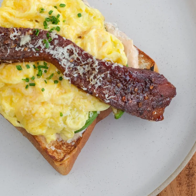 Soft scrambled eggs and thick-cut bacon over toast